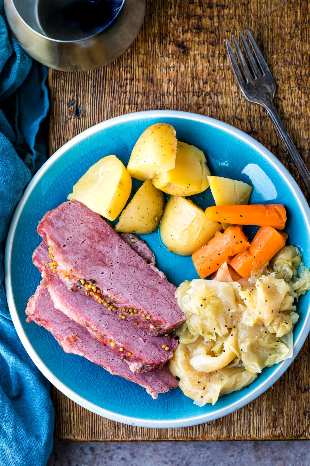 Three slices of corned beef on a plate next to potatoes and cabbage.