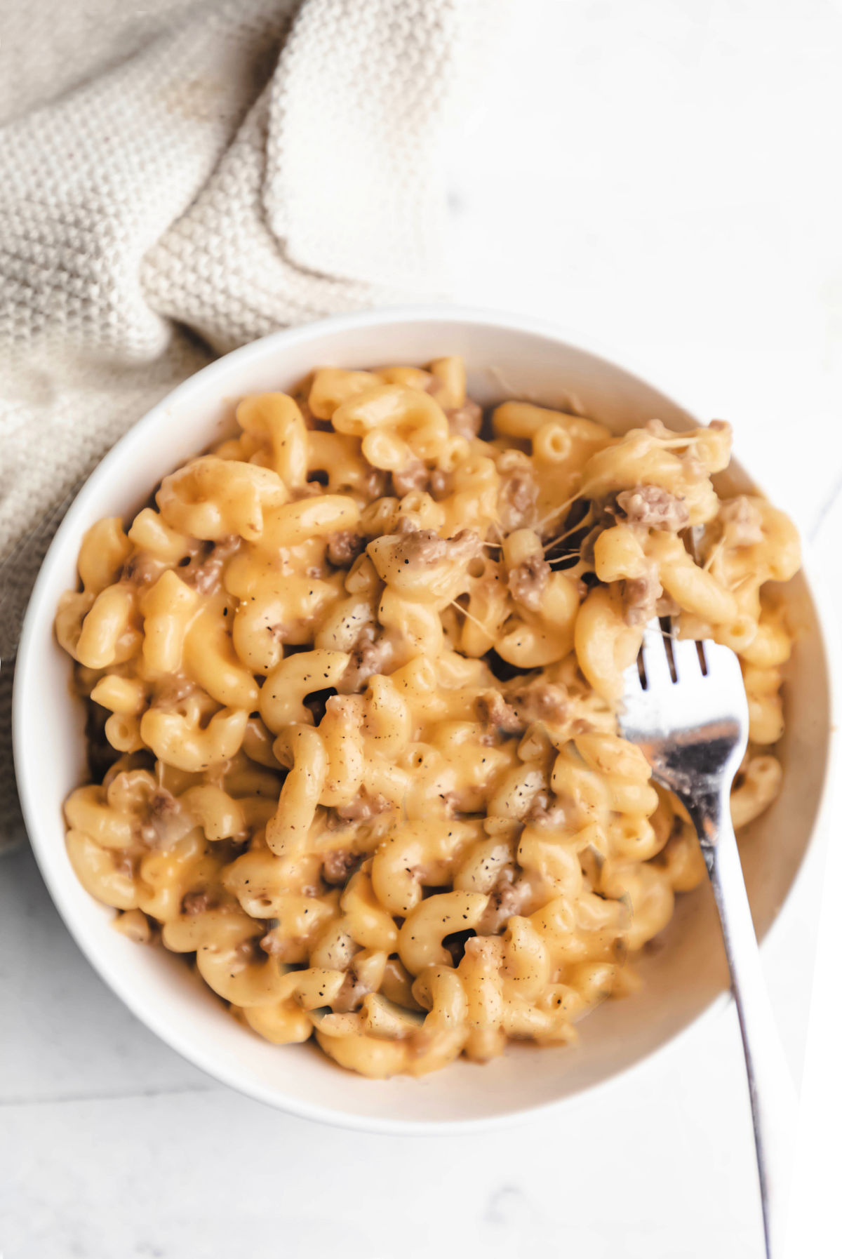 A white bowl of Instant Pot cheeseburger macaroni with a fork in it. 