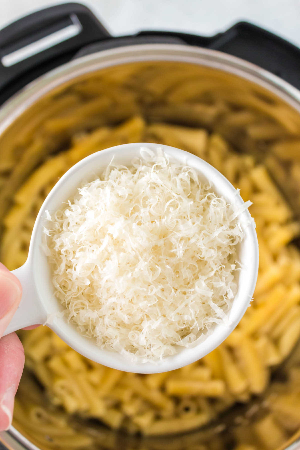 A measuring cup of grated parmesan cheese over an instant pot. 