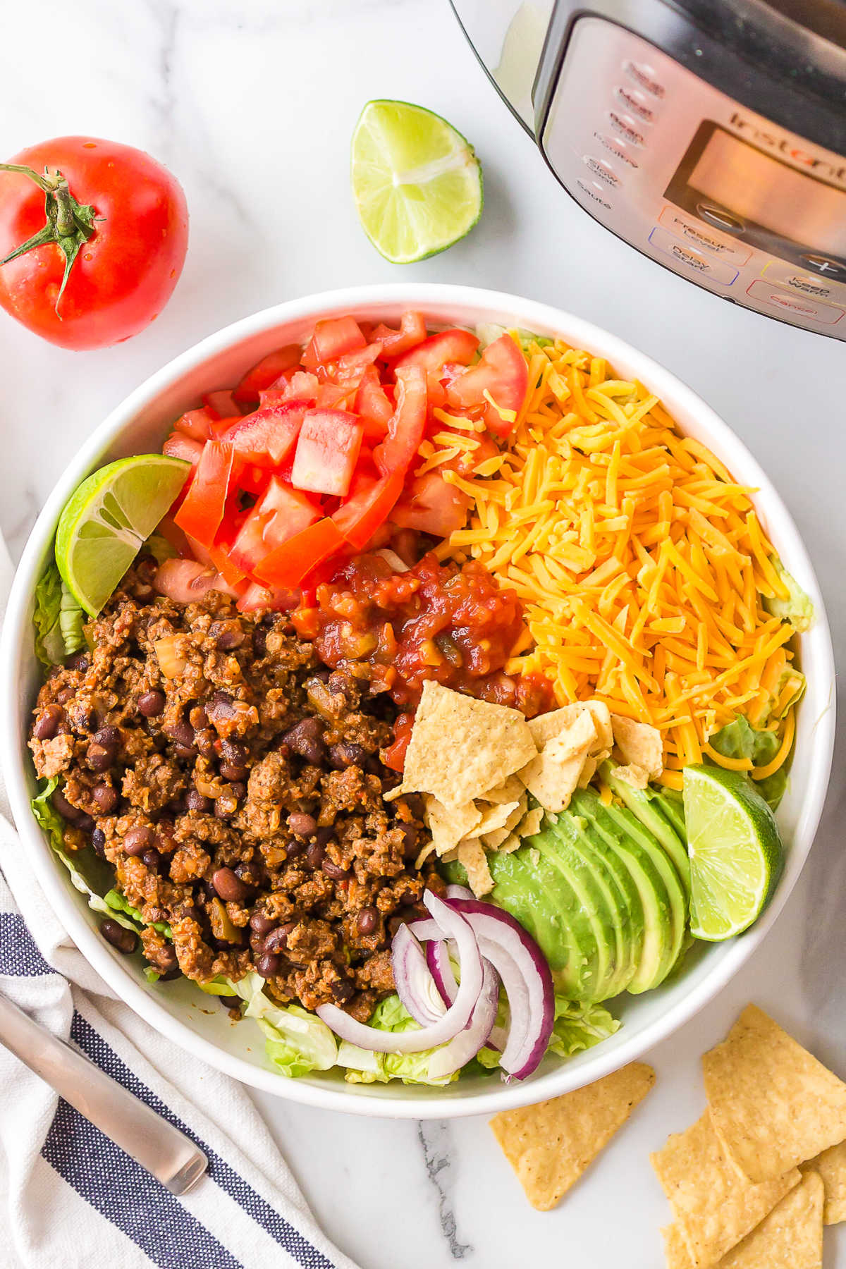 Taco salad in a white dish next to an Instant Pot. 
