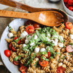 Caprese pasta salad with wooden salad tongs in it.