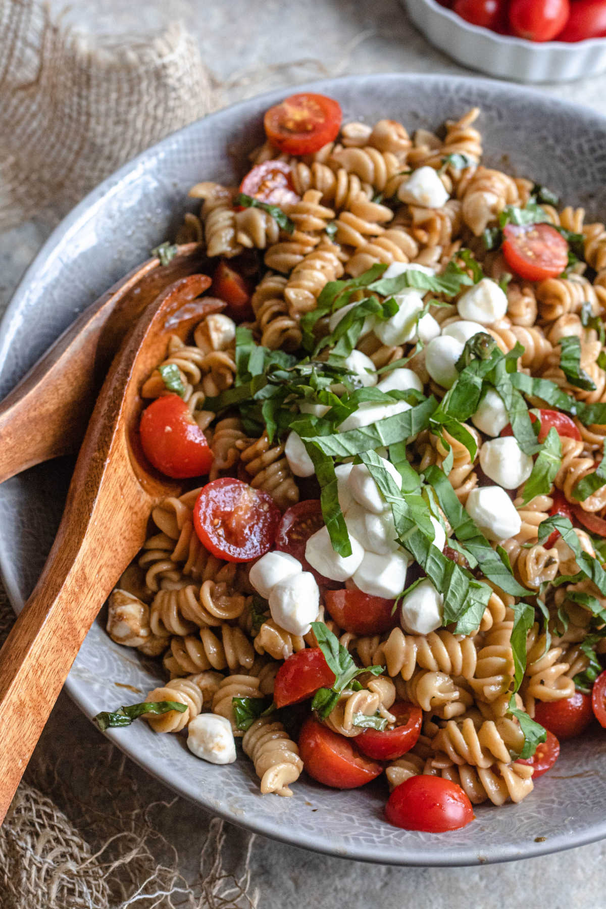 Caprese pasta salad in a gray bowl topped with fresh basil. 
