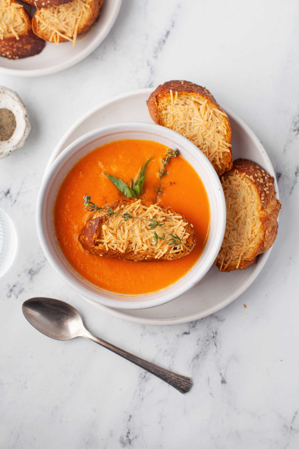 A slice of cheese topped baguette in a bowl of tomato soup. 