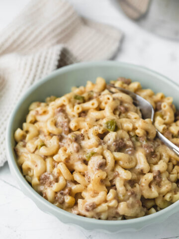 A green dish with Instant Pot Philly cheesesteak pasta and a silver fork in it.