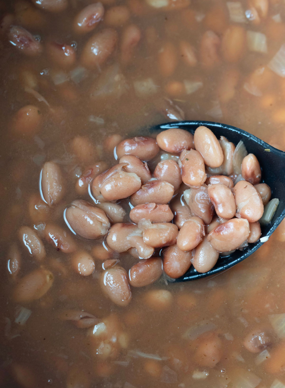 A black spoon lifting beans out of an Instant Pot. 