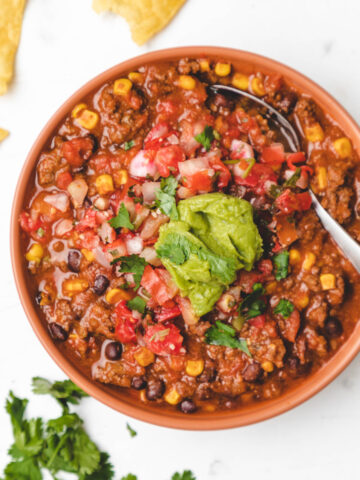 A bowl of Instant Pot beef and black bean chili topped with cilantro and a scoop of guacamole.
