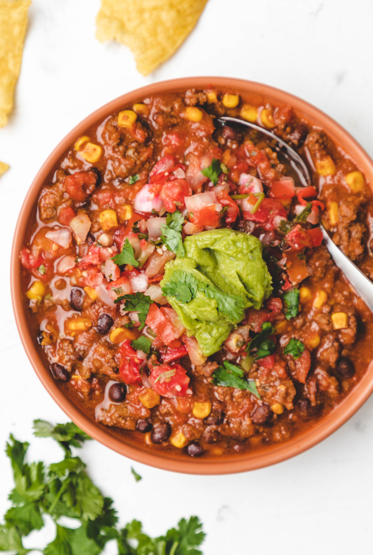 A bowl of Instant Pot beef and black bean chili topped with cilantro and a scoop of guacamole. 