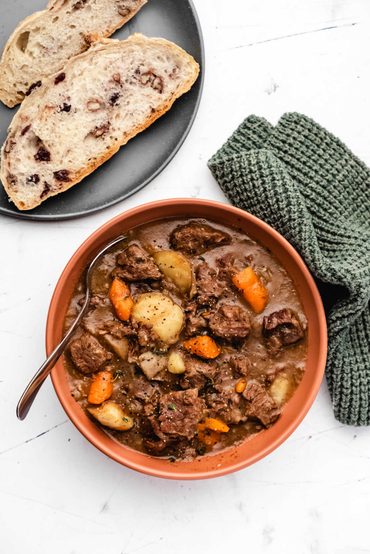 A bowl of instant pot beef stew next to a plate with two slices of cranberry nut bread. 