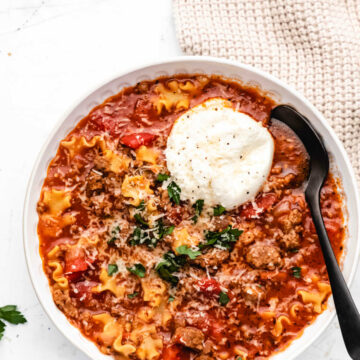 A bowl of lasagna soup with a scoop of ricotta and parsley on top.