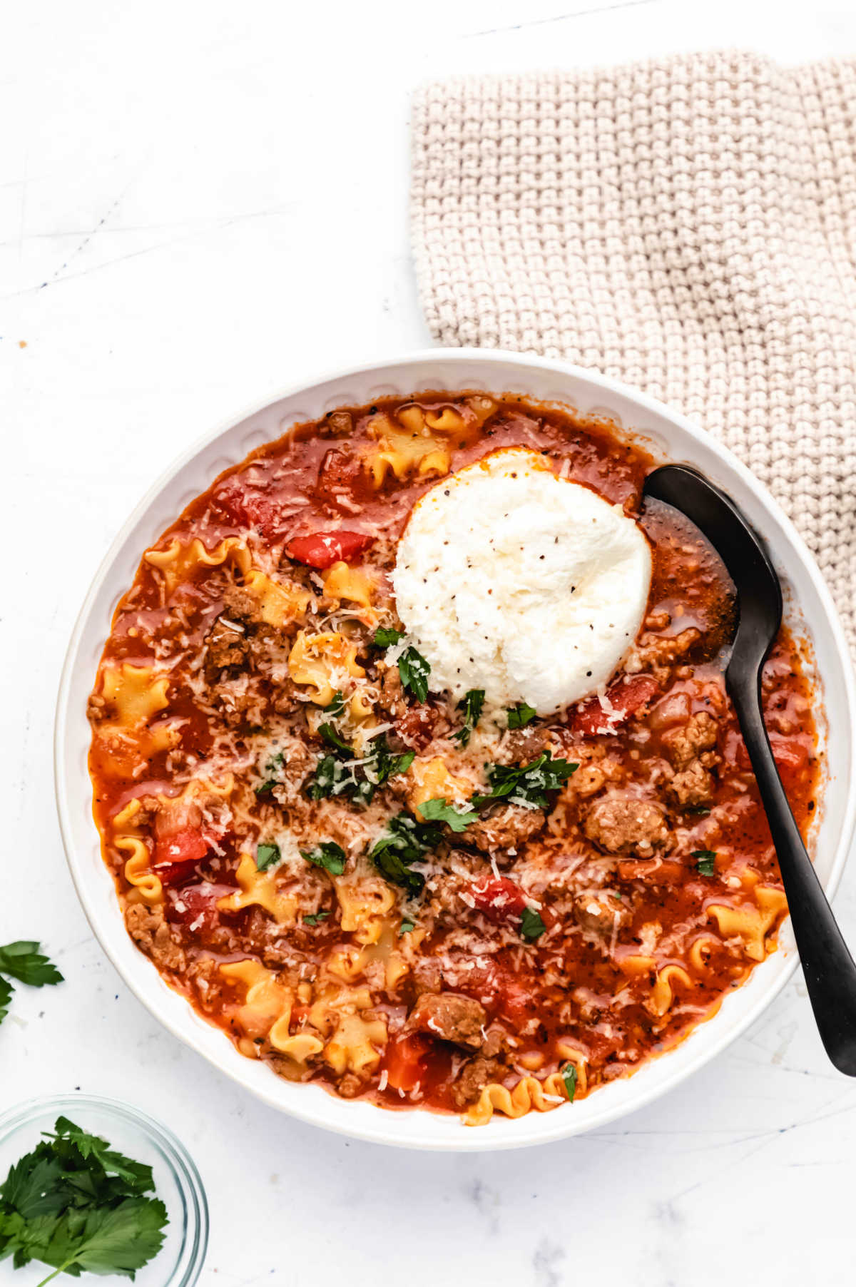 A bowl of lasagna soup with a scoop of ricotta and parsley on top. 