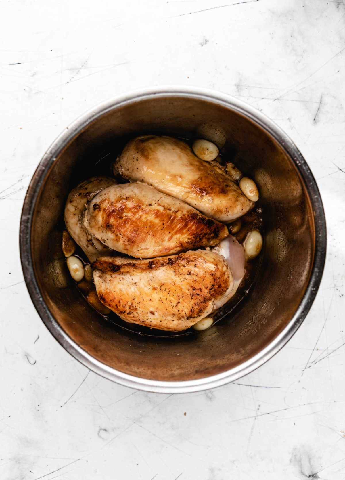 seared chicken breast with garlic cloves in an instant pot inner pot. 
