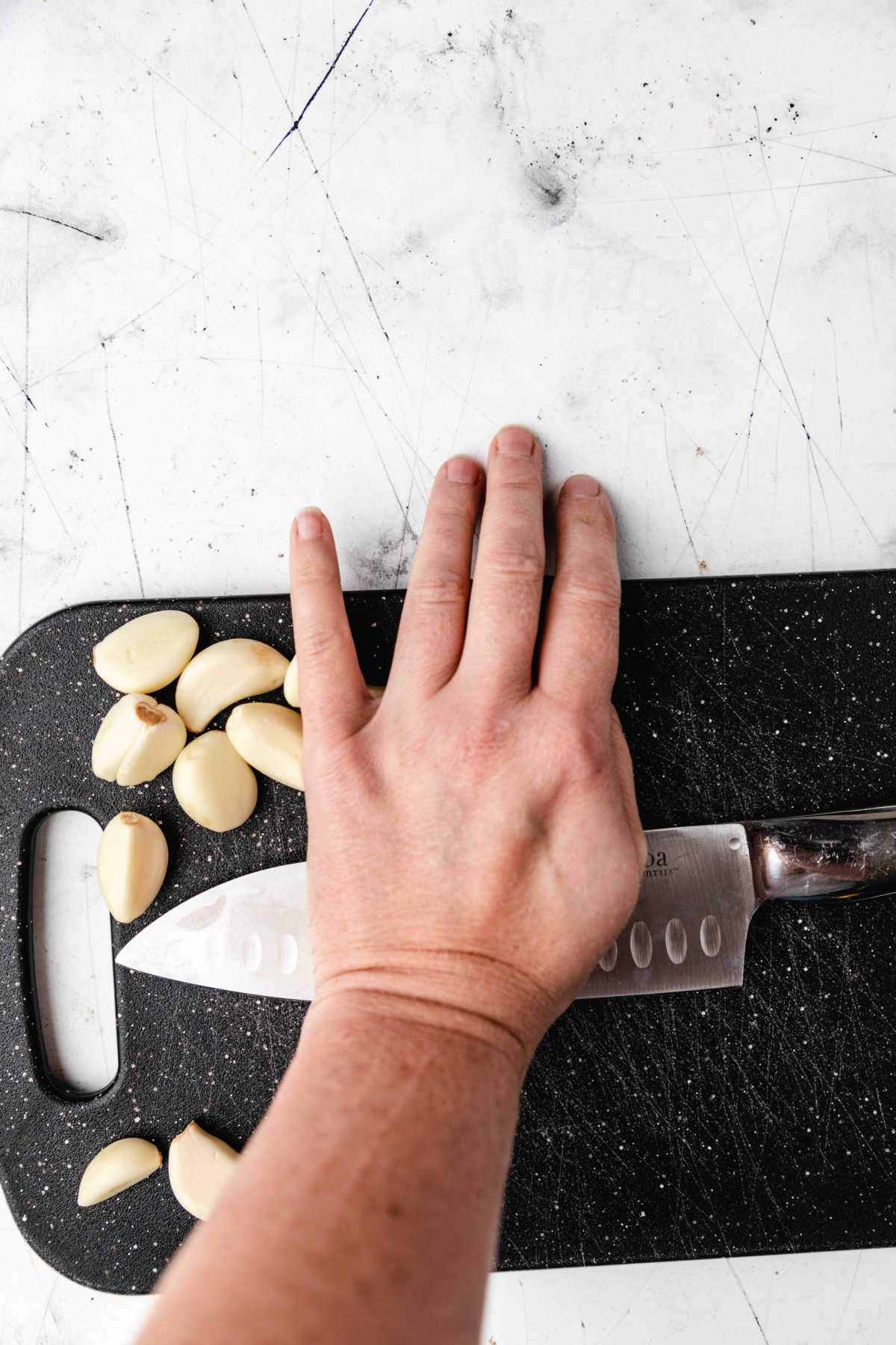 A hand pressing down on a knife to smash a clove of garlic. 