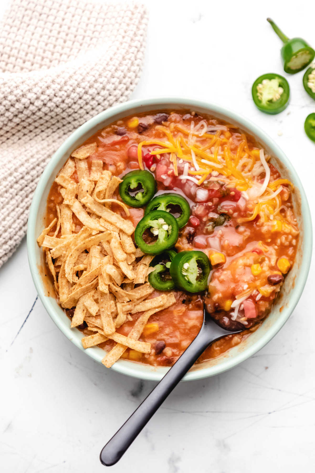 A bowl of vegetarian tortilla soup topped with sliced jalapenos, cheese and tortilla strips. 
