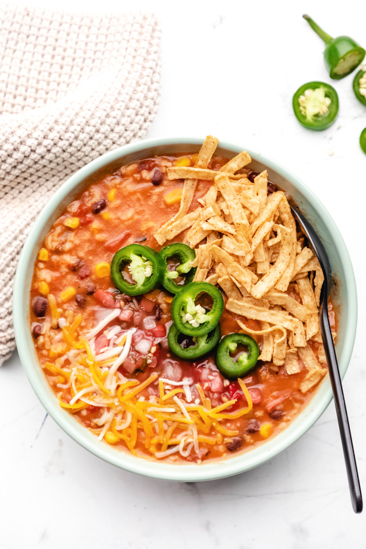 A bowl of vegetarian tortilla soup topped with tortilla strips, sliced jalapenos, and shredded cheese. 
