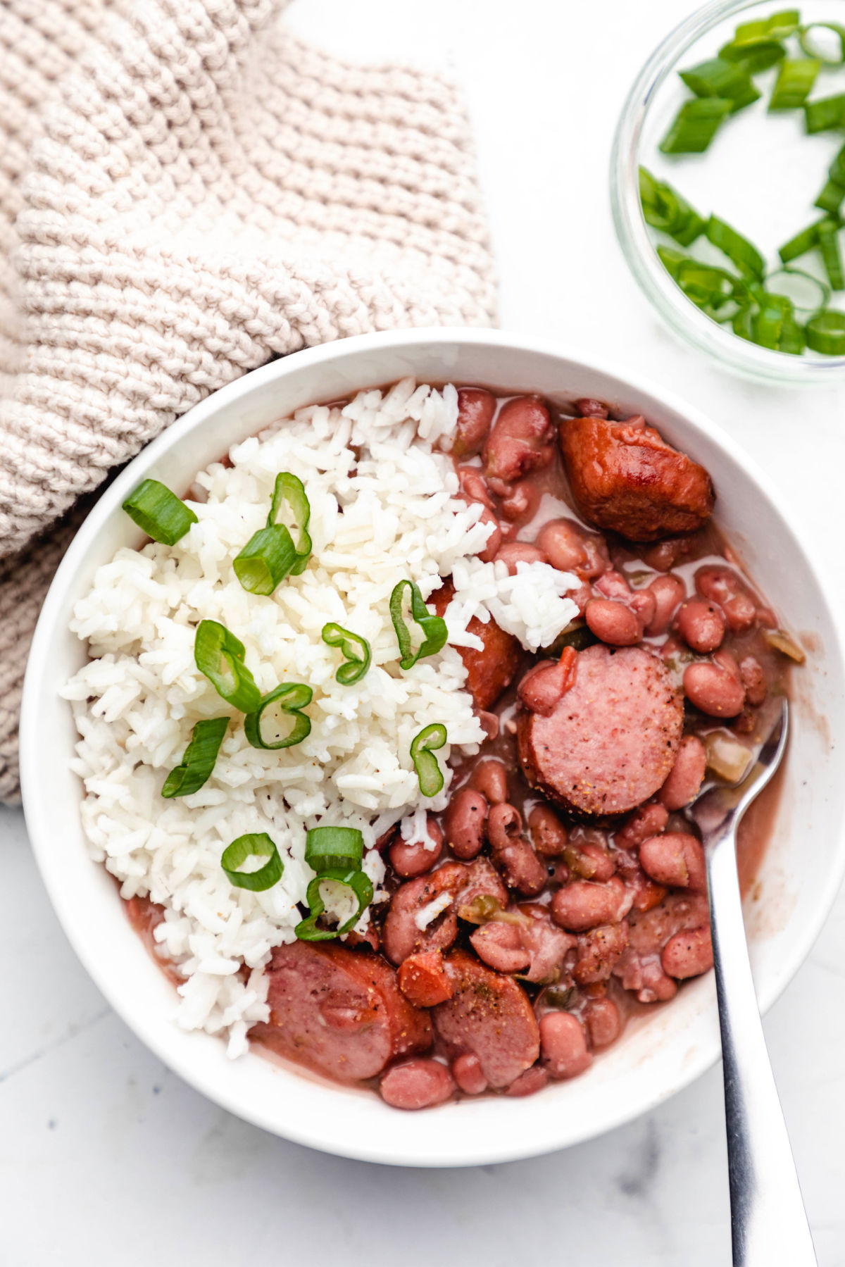 A white bowl of red beans and rice with a silver fork in it.  