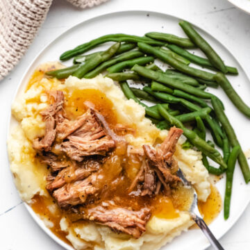 Instant Pot French onion pot roast over mashed potatoes on a white plate.