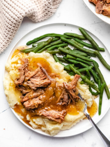 Instant Pot French onion pot roast over mashed potatoes on a white plate.