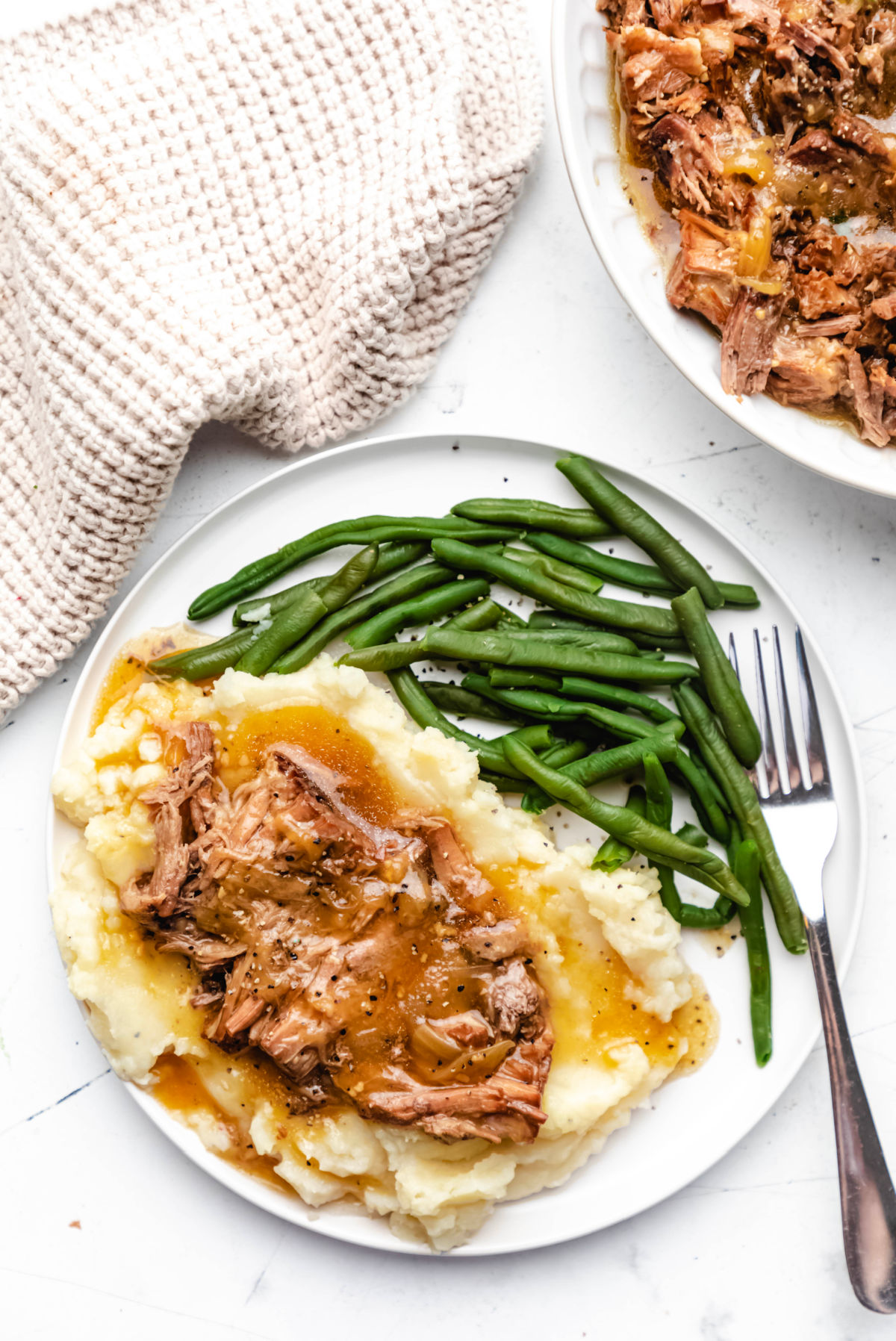 A plate with green beans mashed potatoes and French onion pot roast on it.