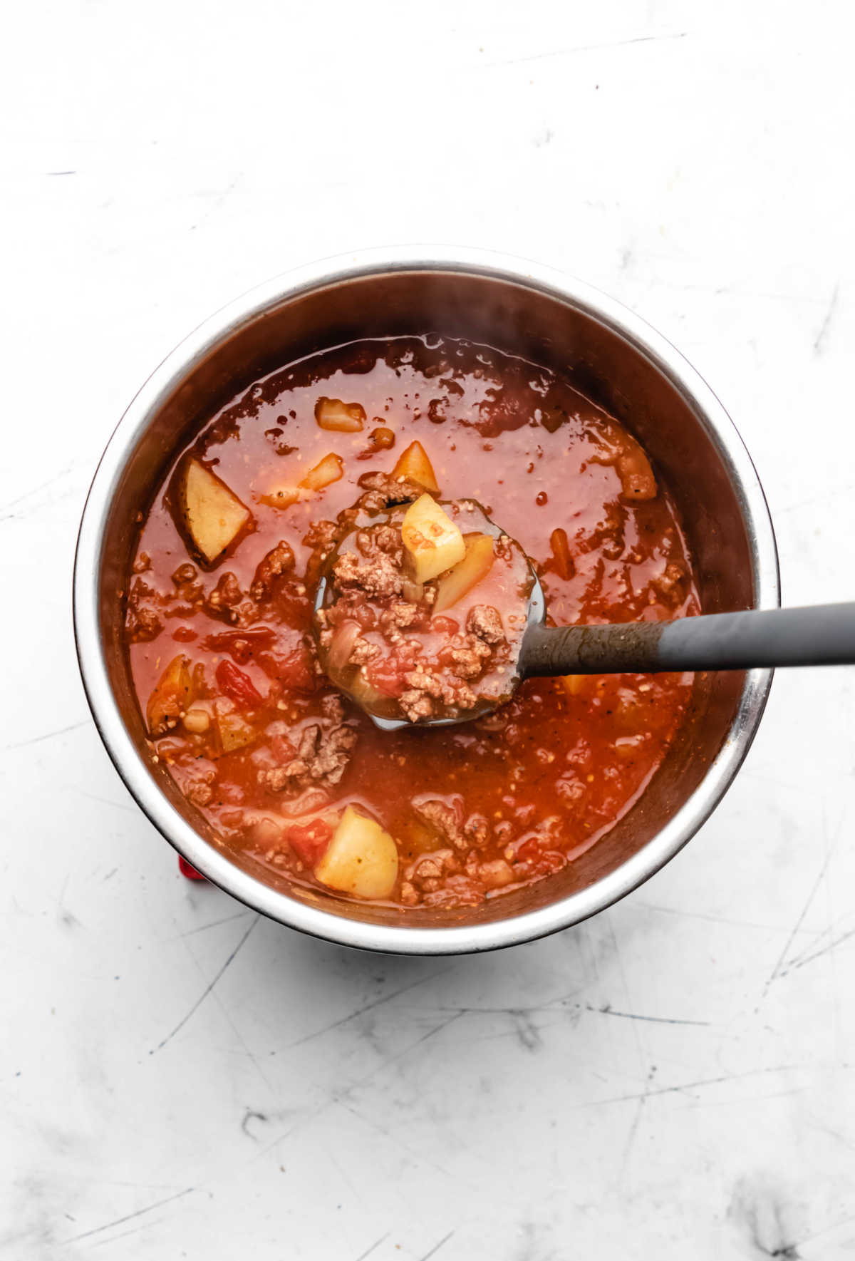 A ladle scooping up hamburger soup from an instant pot inner pot. 