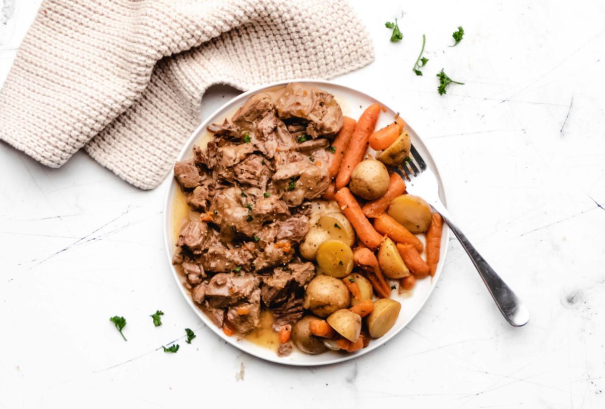 A plate of ranch beef tips and potatoes and carrots with a fork on it. 
