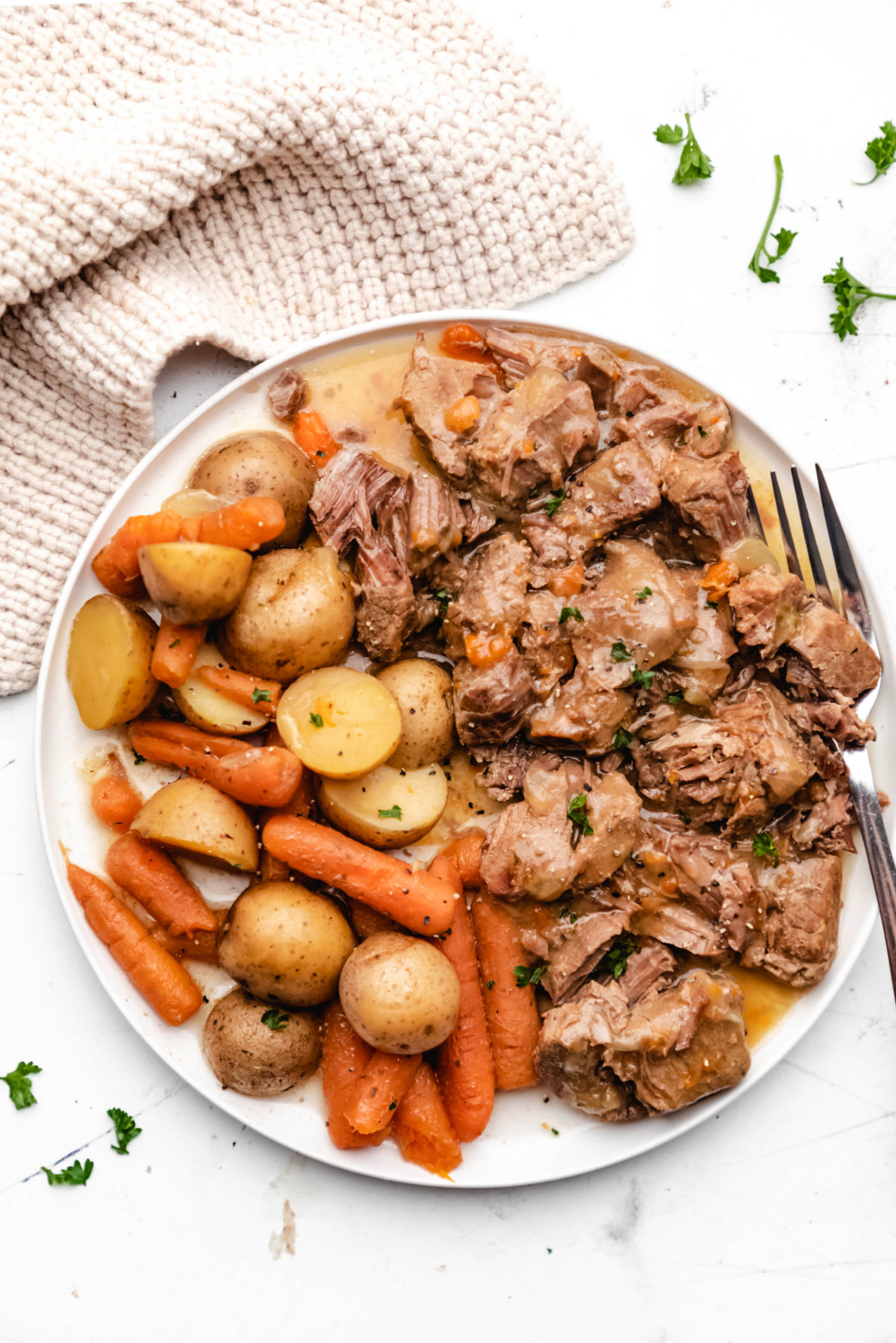 A plate of ranch beef tips, potatoes, and carrots next to a knit napkin.