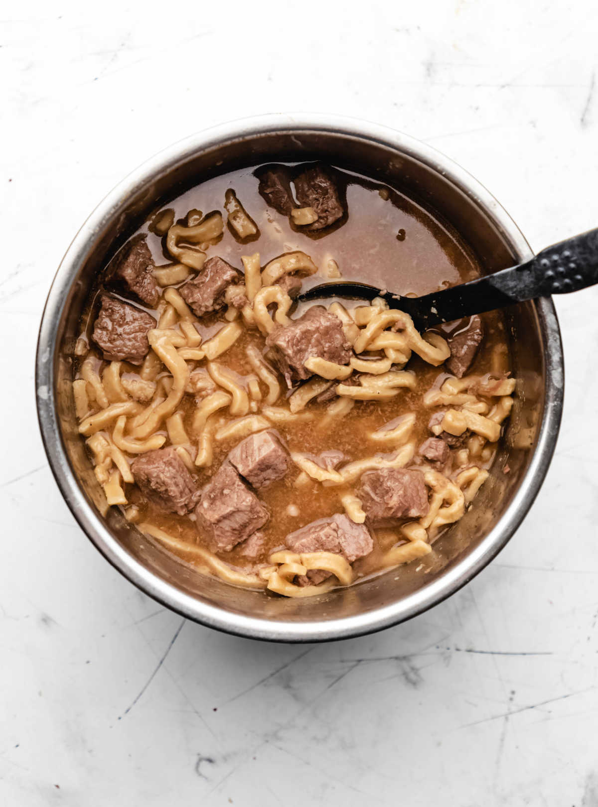 A black spoon stirring beef and noodles in an Instant Pot. 