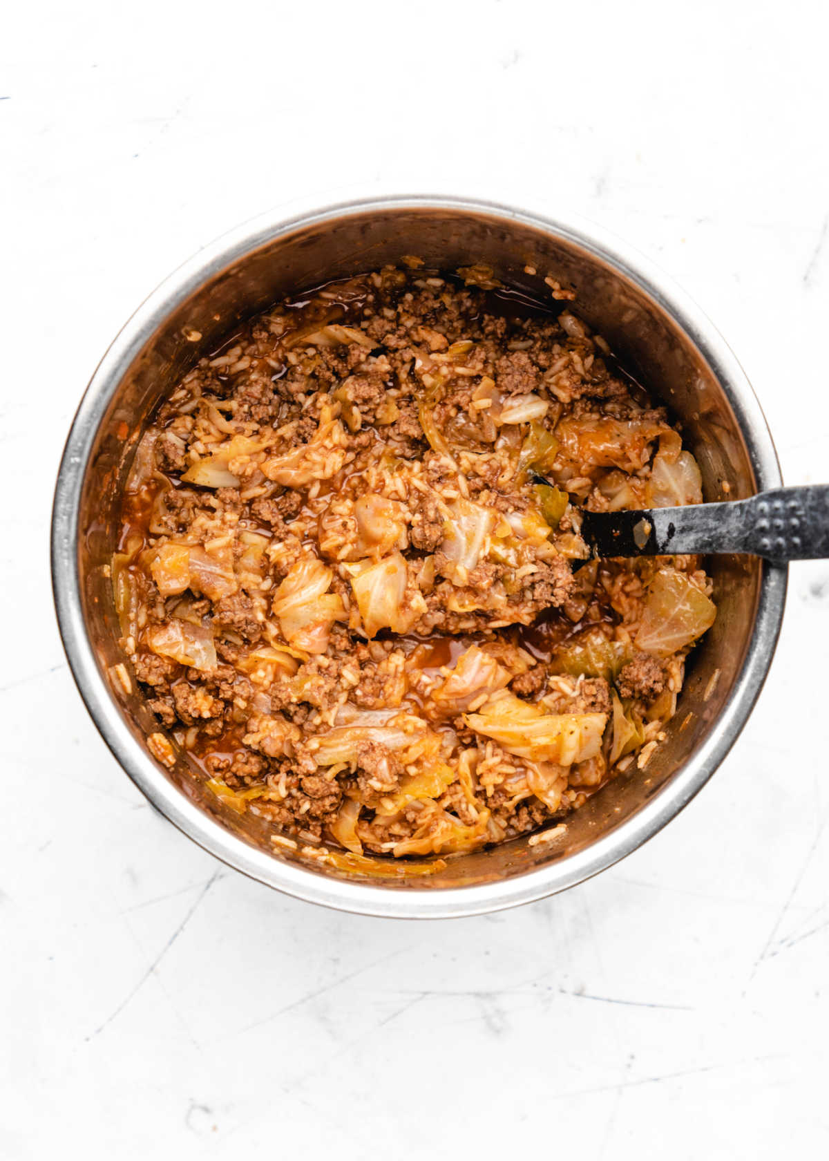 A black spoon stirring unstuffed cabbage rolls in an Instant Pot. 