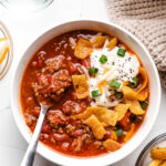 A bowl of easy instant pot beef chili next to dishes of green onions and cheese.