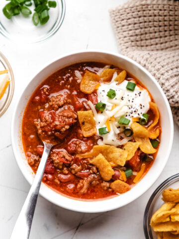 A bowl of easy instant pot beef chili next to dishes of green onions and cheese.