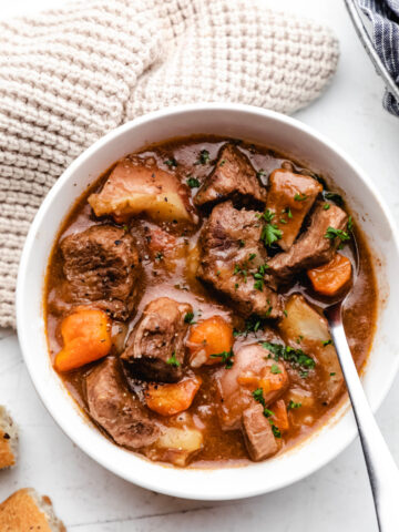 A bowl of Irish beef stew with a silver spoon in it.