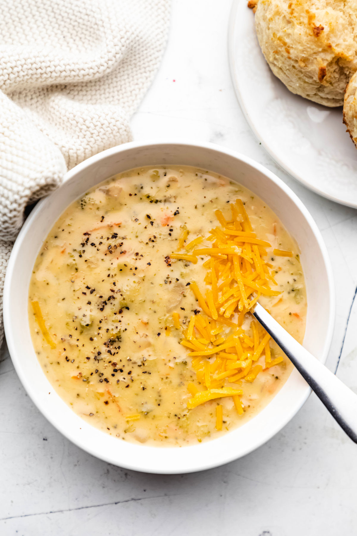 A bowl of Instant Pot broccoli cheddar soup next to a plate of biscuits. 