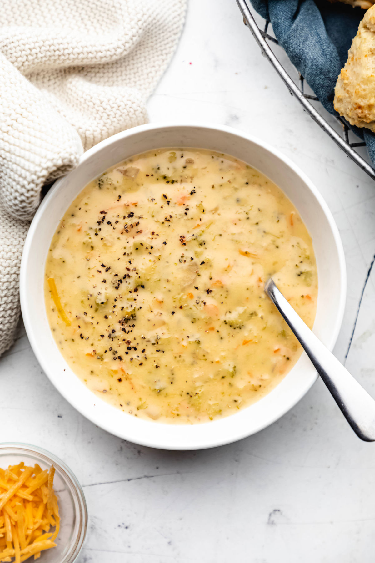 A white bowl of Instant Pot broccoli cheese soup next to a dish of cheese. 