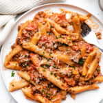A white plate with instant pot ground beef pasta topped with parmesan and parsley.