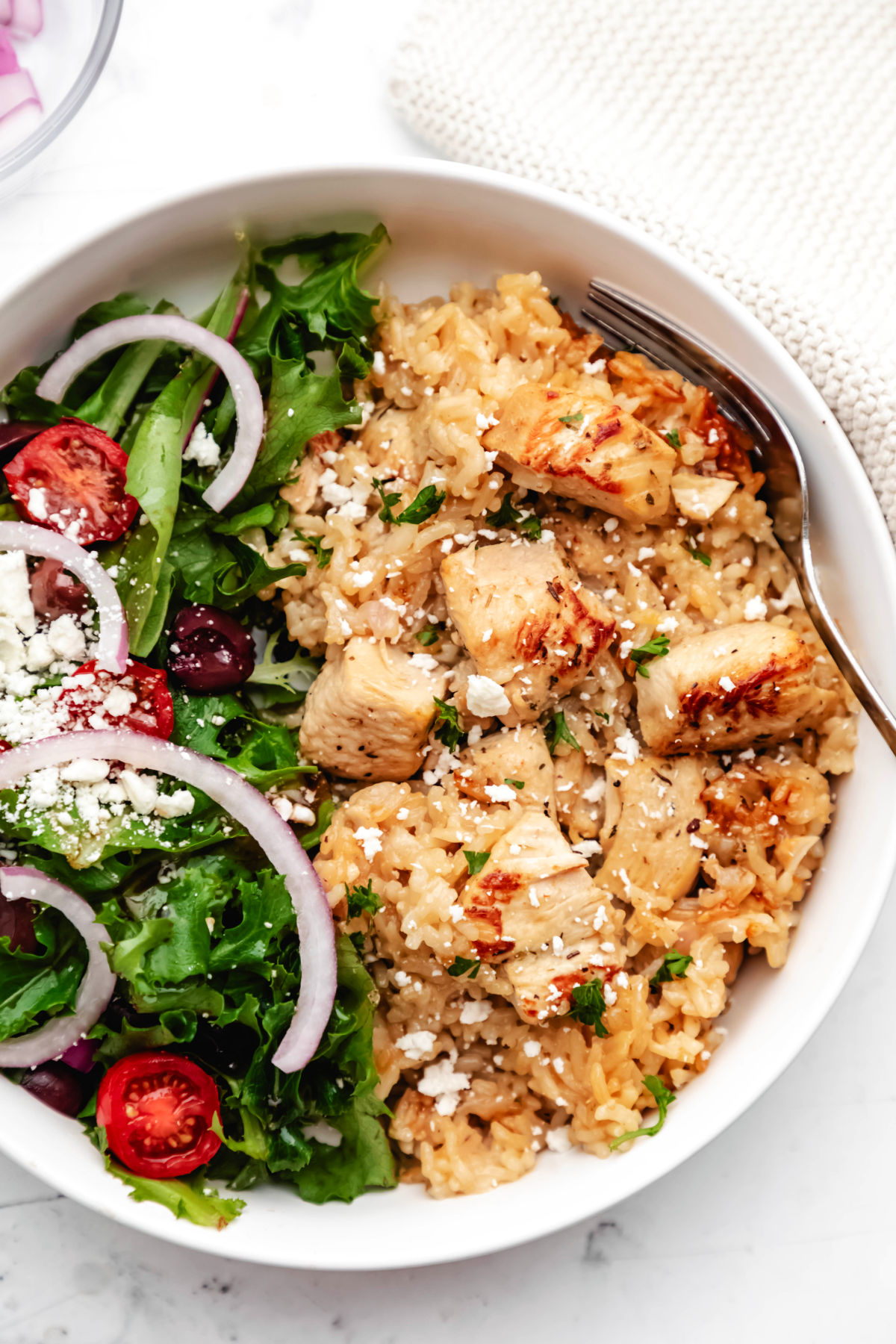 Instant Pot Greek chicken and rice next to a Greek salad in a large white dish.