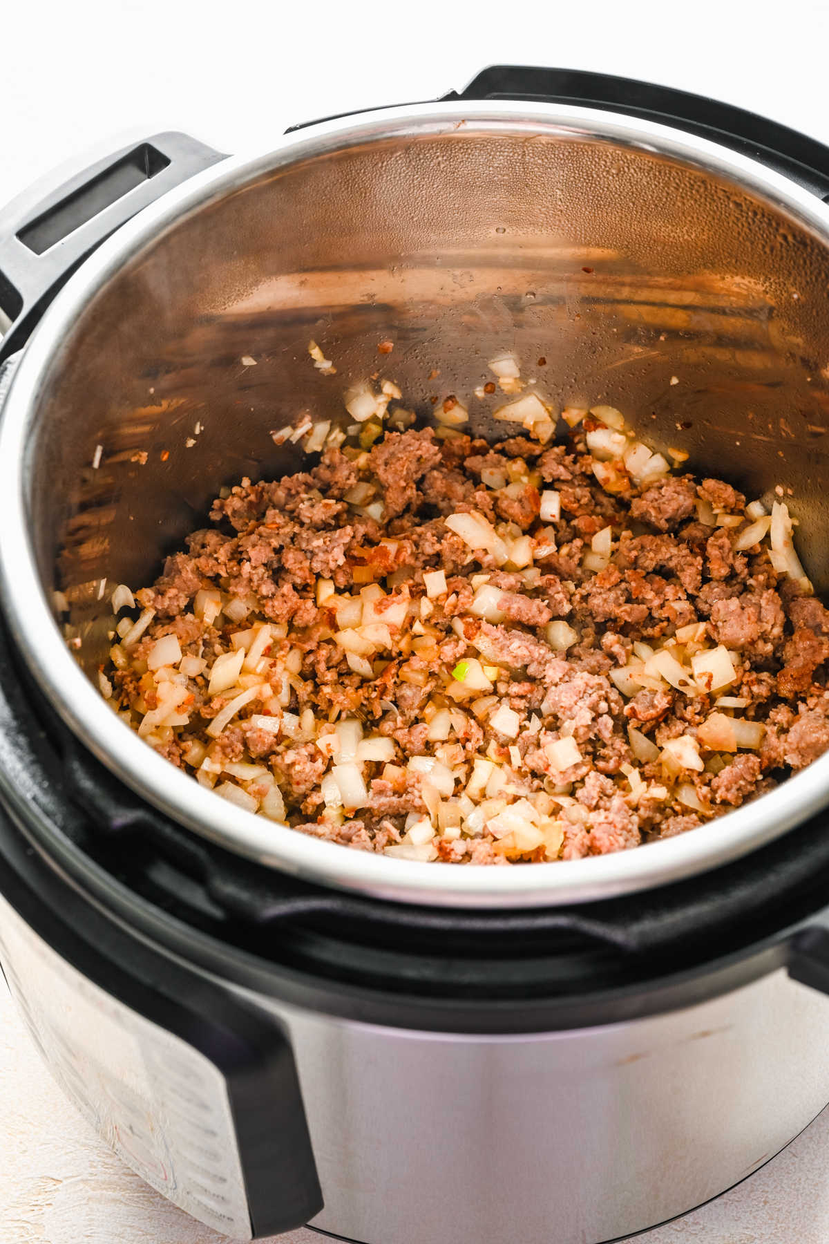 Browned Italian sausage and diced onion in an Instant Pot.