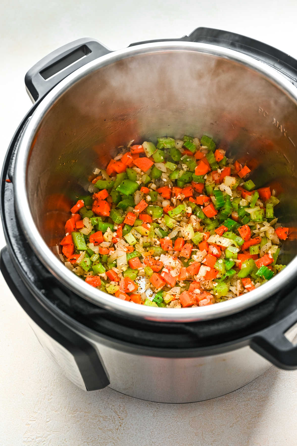 Italian seasoning and pepper on top of sauteed vegetables in an Instant Pot.