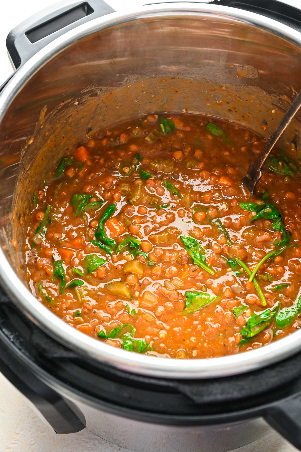 A spoon stirring spinach into lentil soup in an Instant Pot. 