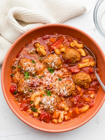 A bowl of Instant Pot meatball soup next to a cream knit kitchen towel.