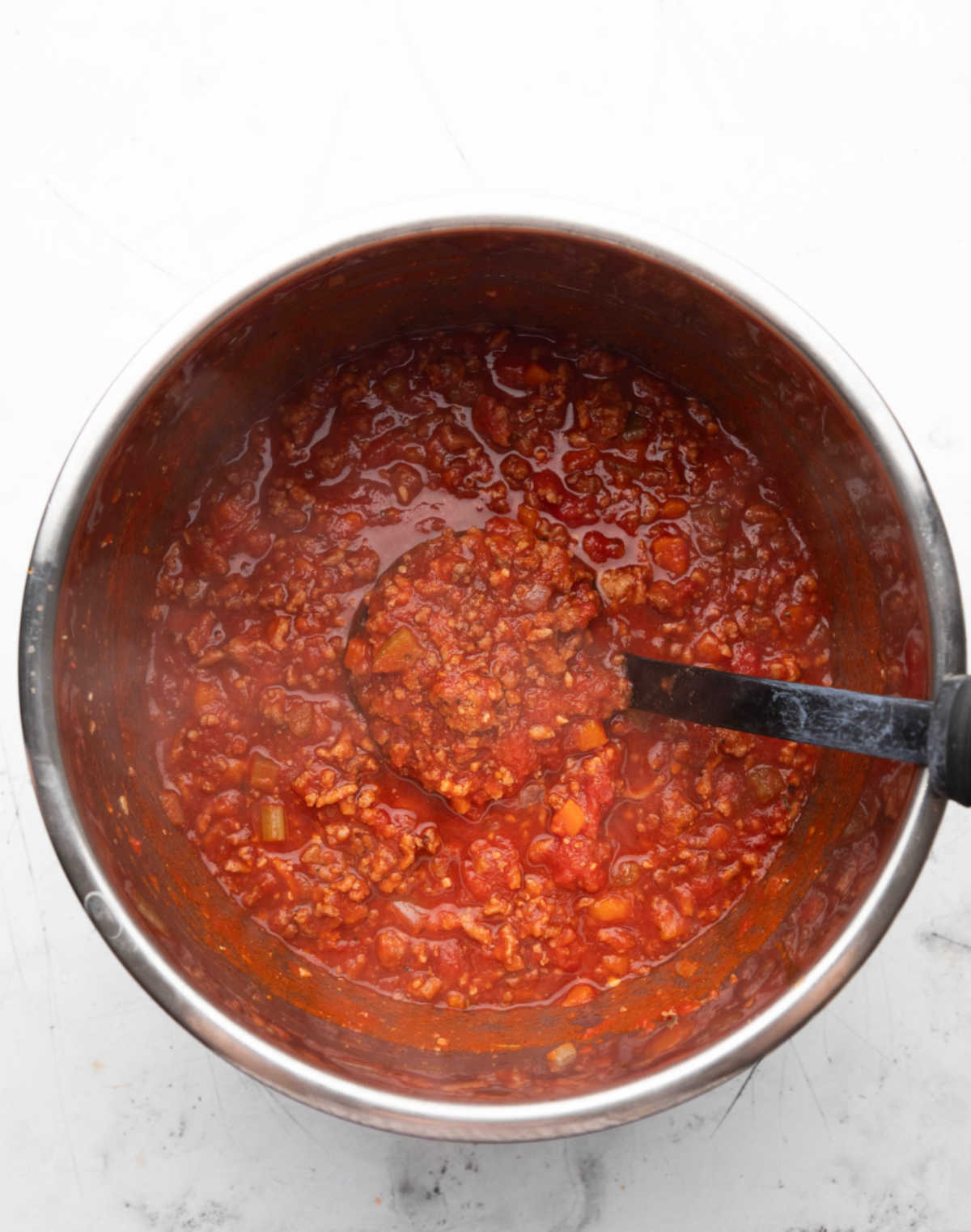 A black ladle holding a scoop of hot Instant Pot bolognese in a pot.