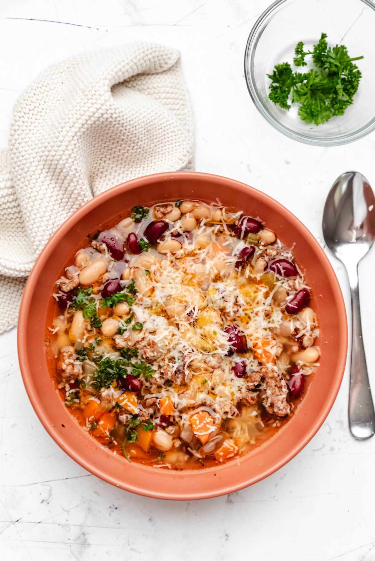 A silver spoon and a dish of parsley next to a bowl of Instant Pot bean soup.