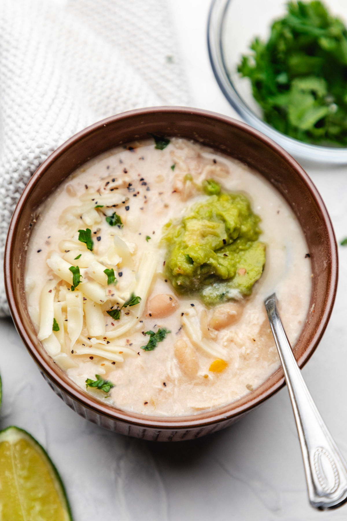 Top view of a brown bowl of Instant Pot white chicken chili between a dish of cilantro and a fresh lime wedge.