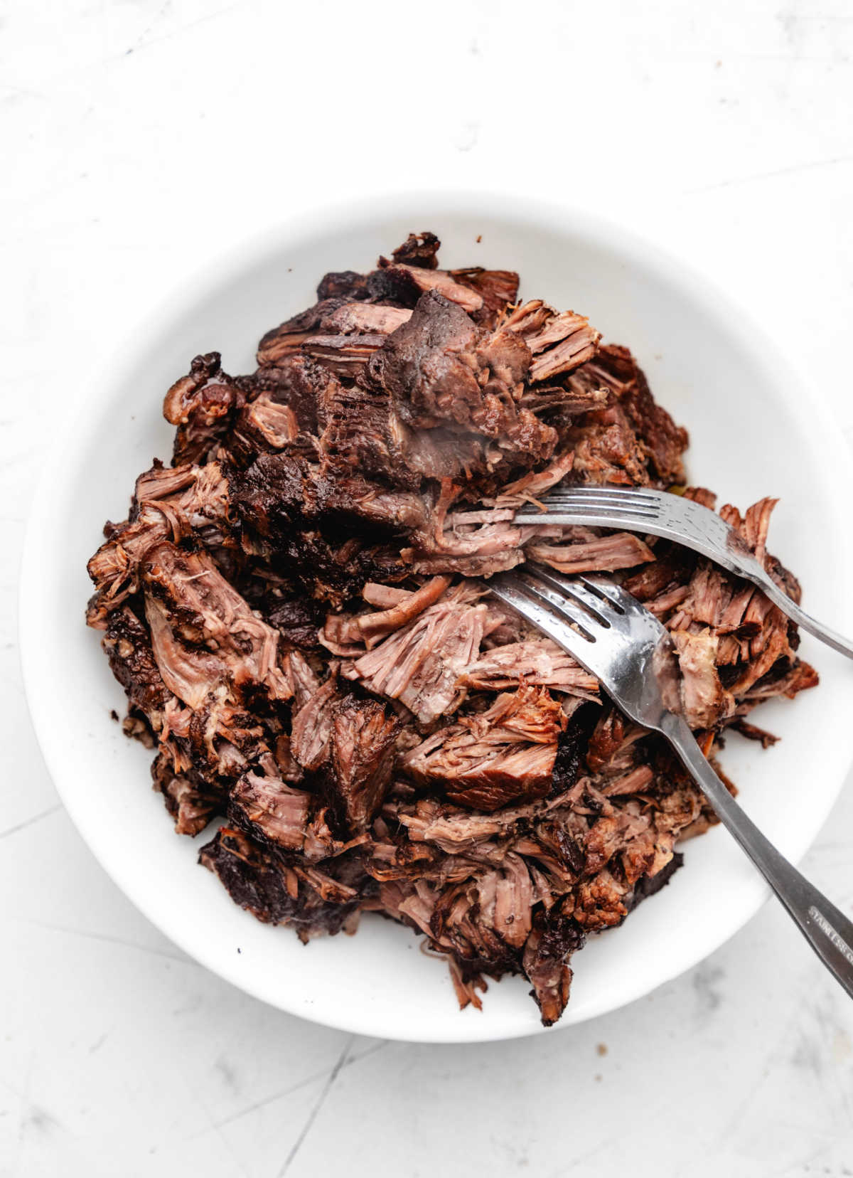 Two forks shredded balsamic beef on a white plate. 