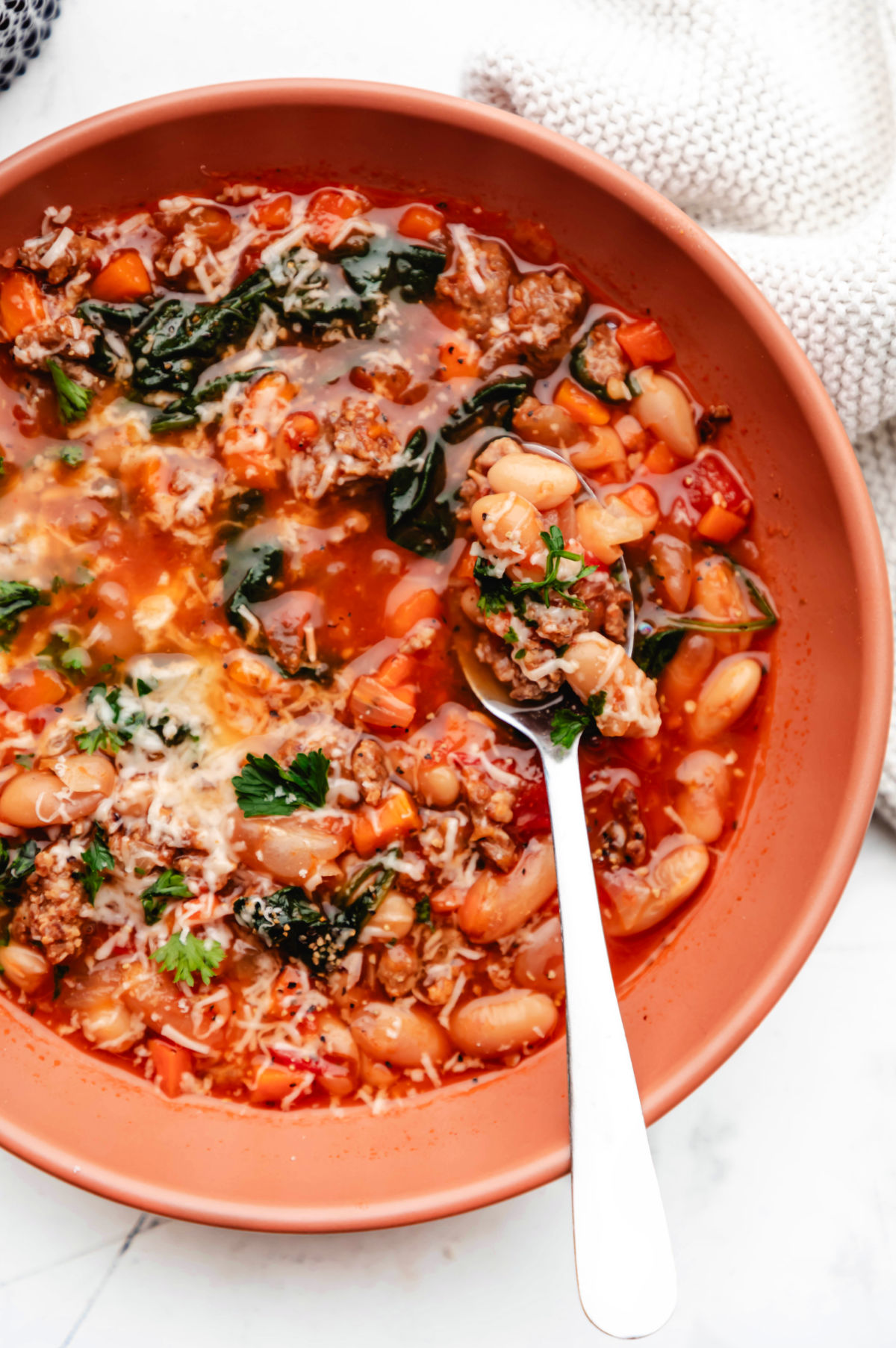 Close up photo of a bowl of Italian sausage and bean soup in a terracotta colored bowl. 