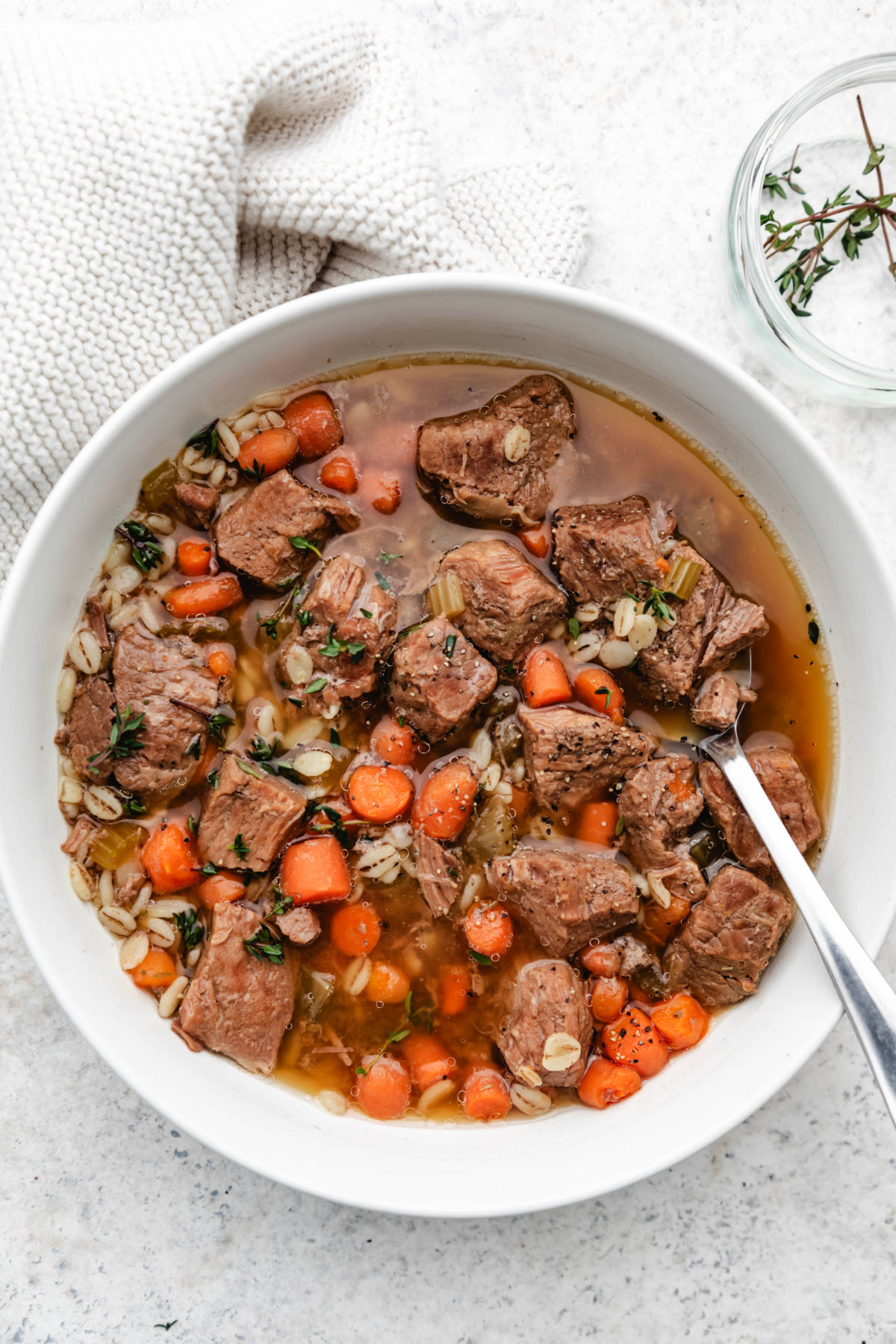 A bowl of Instant Pot beef and barley soup next to a dish of fresh thyme.