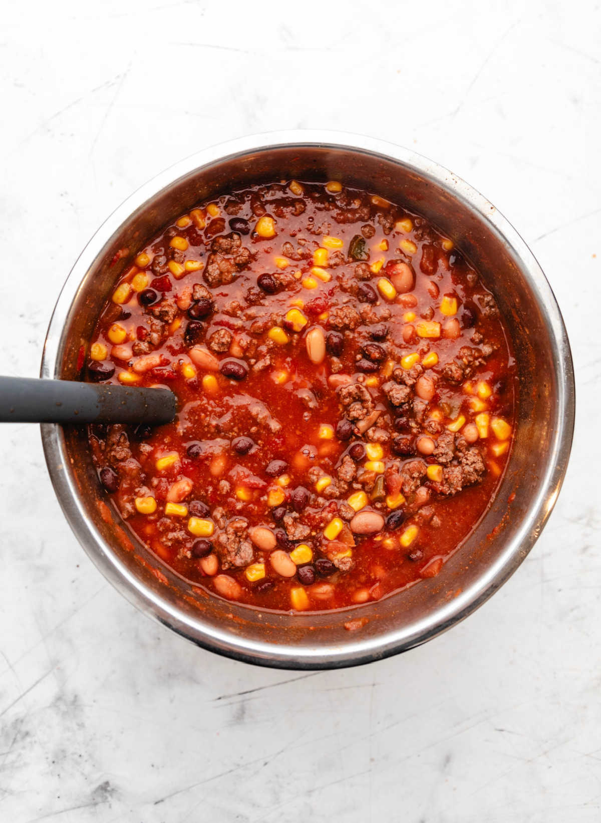 A black spoon stirring frozen corn into an Instant Pot full of taco soup.