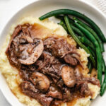 A plate of Instant Pot mushroom pot roast on top of mashed potatoes.
