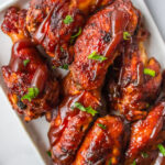 A white tray of Instant Pot BBQ chicken wings topped with sliced green onions.