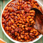 A bowl of Instant Pot baked beans next to a plate of dinner rolls.