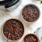 Three dishes of black beans next to an Instant Pot.