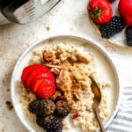 A bowl of oats topped with fresh sliced strawberries and blackberries next to an Instant Pot.